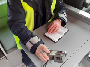 w radiowozie, przy stoliku, siedzi policjant ruchu drogowego, który trzyma alkotest. Na stoliku leży zapisany notatnik służbowy