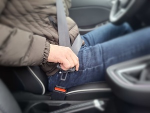 za kierownicą samochodu siedzi mężczyzna, który jest w trakcie zapinania pasów bezpieczeństwa