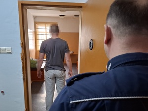 w celi stoi mężczyzna. Za nim przy drzwiach stoi policjant służby dyżurnej
