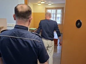 w celi stoi mężczyzna. Za nim przy drzwiach stoi policjant służby dyżurnej