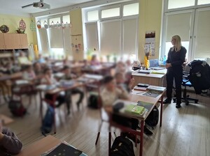 klasa szkolna. Przy biurku nauczyciela stoi policjantka. W ławkach siedzą pierwszoklasiści