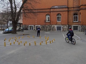 na placu szkolnym policjantka ruchu drogowego obserwuje chłopca jadącego rowerem