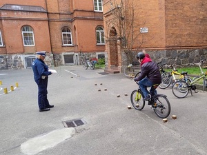 na placu szkolnym policjantka ruchu drogowego obserwuje chłopca jadącego rowerem po torze przeszkód