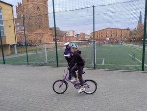 na placu szkolnym policjantka ruchu drogowego obserwuje dziewczynkę jadącą rowerem