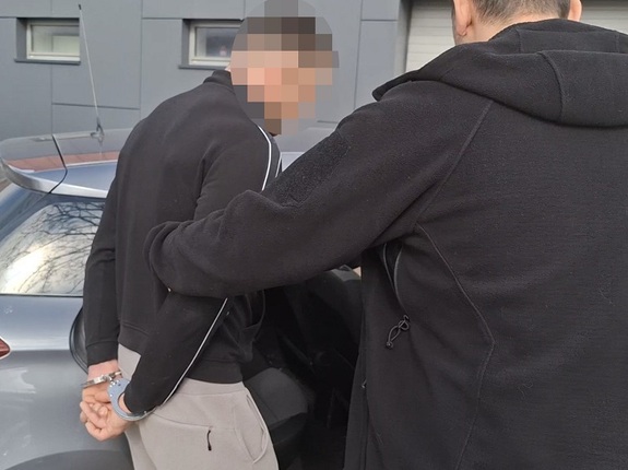 policjant kryminalny wprowadza na tylne siedzenie nieoznakowanego radiowozu mężczyznę, który ma ręce skute za plecami kajdankami