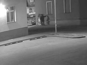 czarno białe ujęcie z kamery monitoringu. Przy ścianie budynku stoi mężczyzna, który nanosi na elewację napis