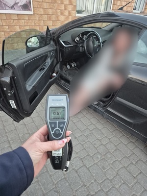 w samochodzie na miejscu kierowcy siedzi kobieta. Przed nią stoi policjantka, która trzyma w ręce alkotest z wyświetlonym wynikiem badania 0,57 mg/l