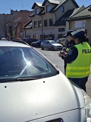 w strefie zamieszkania na targowisku miejskim przy osobowym samochodzie stoją policjantka ruchu drogowego i strażniczka miejska