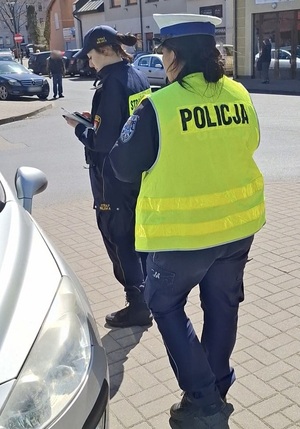 w strefie zamieszkania na targowisku miejskim przy osobowym samochodzie stoją policjantka ruchu drogowego i strażniczka miejska