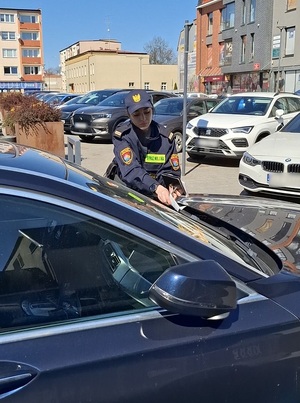 w centrum miasta, za wycieraczki osobowego samochodu strażniczka miejska wkłada wezwanie do stawiennictwa w związku z nieprawidłowym parkowaniem