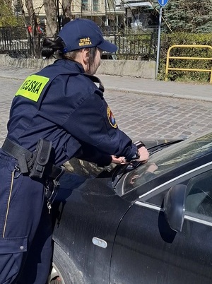 strażnicza miejska wkłada za wycieraczki samochodu wezwanie