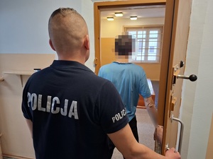w otwartych drzwiach celi stoi zatrzymany mężczyzna. Za nim stoi policjant służby dyżurnej