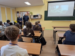 w szkolnej klasie, przed siedzącymi w ławkach uczniami stoją policjantka i policjant