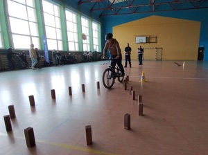 w sali gimnastycznej uczeń pokonuje na rowerze tor przeszkód wyznaczony pachołkami. Obserwują go policjant i policjantka ruchu drogowego