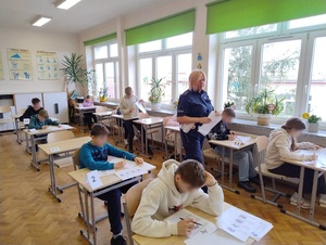 w klasie szkolnej uczniowie rozwiązują test. Pomiędzy ławkami chodzi policjantka ruchu drogowego