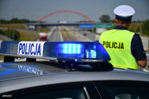 policjant ruchu drogowego stojący na drodze przy radiowozie z włączonymi sygnałami błyskowymi