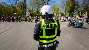 Na ulicy stoi policjant ruchu drogowego, który obserwuje uczestników przemarszu