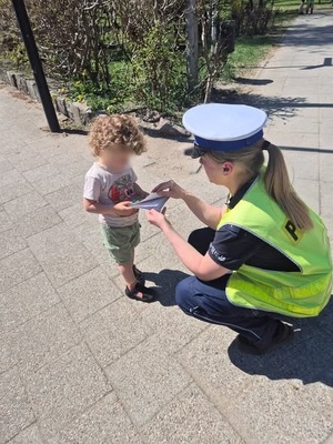 policjantka ruchu drogowego przekazuje małemu chłopcu książeczkę profilaktyczną