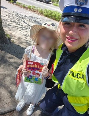 zdjęcie uśmiechniętej policjantki ruchu drogowego i dziewczynki, która trzyma książeczkę profilaktyczną o znakach drogowych