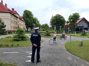 miasteczko ruchu drogowego na terenie Komendy Powiatowej Policji w Lęborku. Policjant ruchu drogowego obserwuje dwoje uczniów jadących rowerami