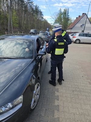 dwaj policjanci ruchu drogowego stoją przy osobowym audi od strony kierowcy. Jeden przykłada do szyby samochodu urządzenie pomiarowe