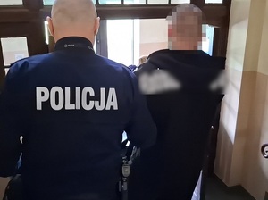policjant prowadzi zatrzymanego mężczyznę schodami w dół w kierunku wyjścia z budynku komendy