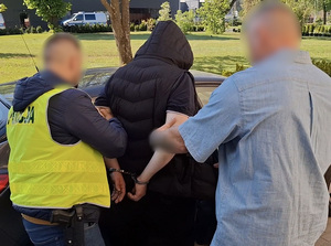 dwaj policjanci służby kryminalnej wprowadzają na tylne siedzenie nieoznakowanego radiowozu mężczyznę, który ma ręce skute za plecami kajdankami