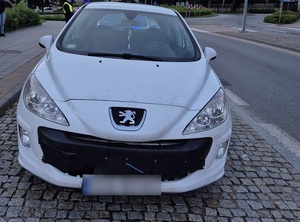 na drodze stoi biały osobowy Peugeot. Za nim stoi policjantka ruchu drogowego