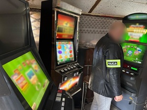 w małym pomieszczeniu przy trzech czynnych automatach do gier stoi policjant kryminalny