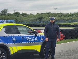 na torze do ćwiczenia jazdy obok oznakowanego radiowozu stoi policjant ruchu drogowego