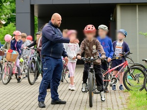 w policyjnym miasteczku ruchu drogowego znajdują się dzieci na rowerach. Przy jednym stoi policjant ruchu drogowego, który wskazuje mu coś ręką