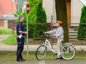 w policyjnym miasteczku ruchu drogowego na oznakowanej drodze znajduje się dziewczynka siedząca na rowerze. Przed nią stoi policjant ruchu drogowego
