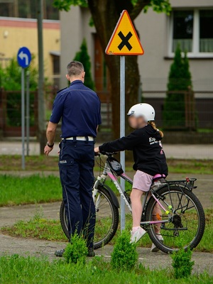 w policyjnym miasteczku ruchu drogowego na oznakowanej drodze znajduje się dziewczynka siedząca na rowerze. Przed nią stoi policjant ruchu drogowego