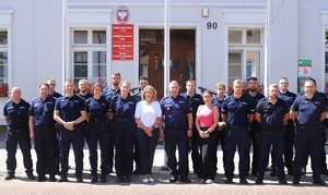 zdjęcie grupowe zrobione przed Urzędem Miejskim w Łebie. Przedstawia policjantów i Burmistrz Łeby oraz pracownicę Urzędu