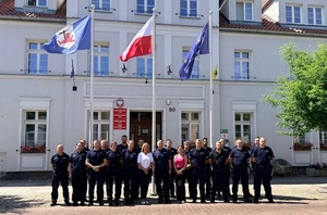 zdjęcie grupowe zrobione przed Urzędem Miejskim w Łebie. Przedstawia policjantów i Burmistrz Łeby oraz pracownicę Urzędu