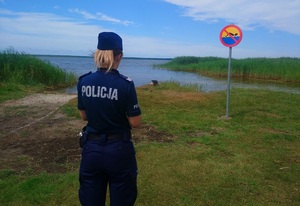 policjantka stojąca przed znakiem z zakazem pływania. W tle jezioro