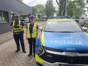 Przy oznakowanym radiowozie stoją policjant i policjantka ruchu drogowego