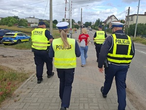 Chodnikiem w stronę przejazdu kolejowego z podniesionym szlabanem idą: dwaj funkcjonariusze SOK, dwoje policjantów ruchu drogowego oraz przedstawicielka PKP
