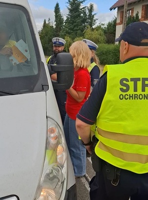 przy samochodzie od strony kierowcy stoją: policjant, funkcjonariusz SOK i przedstawicielka PKP. Kierowca trzyma w dłoni broszurę