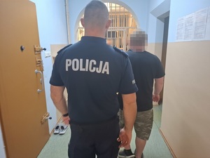 policjant prowadzi korytarzem wzdłuż cel zatrzymanego mężczyznę