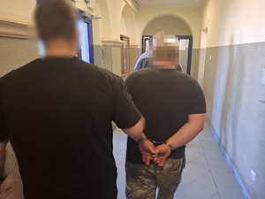 policjant kryminalny prowadzi korytarzem mężczyznę, który ma ręce skute za plecami kajdankami