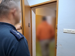 w otwartych drzwiach celi stoi zatrzymany mężczyzna. Przed drzwiami stoi policjant służby dyżurnej
