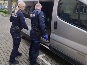 dwoje policjantów służby konwojowej stojących przy otwartych drzwiach nieoznakowanego radiowozu