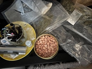 na blacie stoi okrągły metalowy pojemnik wypełniony różowymi tabletkami. Obok leżą dwa przezroczyste worki foliowe wypełnione zbrylonym suszem roślinnym