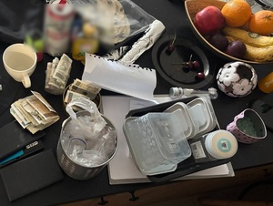 na stole, na którym panuje nieporządek, zastawionym m.in.puszką po piwie, butelką sosu, owocami w paterze, leżą banknoty w polskich nominałach oraz pojemnik w kształcie serca wypełniony niebieskimi kryształkami