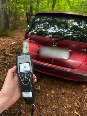 na tle stojącego w lesie osobowego Mercedesa widać trzymany w dłoni alktotest z wyświetlonym wynikiem badania 1,08 mg/l
