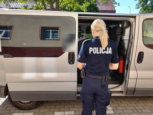 przed nieoznakowanym radiowozem policyjnej służby konwojowej, przy otwartych bocznych rozsuwanych drzwiach stoi policjantka. W aucie widać schylającego się policjanta