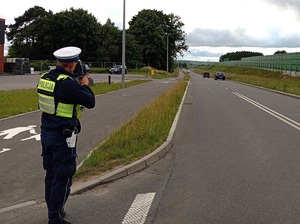 na poboczu drogi stoi policjant ruchu drogowego, który mierzy prędkość przejeżdżających pojazdów za pomocą ręcznego miernika