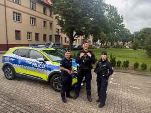 na wewnętrznym placu lęborskiej komendy Policji przy oznakowanym radiowozie Kia stoi troje uśmiechniętych policjantów