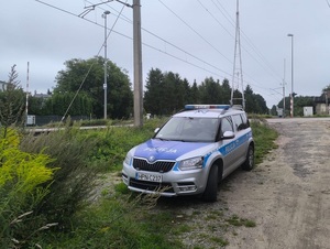 oznakowany policyjny radiowóz Skoda Yeti zaparkowany wzdłuż torów kolejowych nieopodal przejazdu kolejowego
